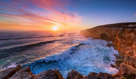 Dramatic sunset over a rugged coastline with crashing waves, reminiscent of the Chairman's July 2026 board meeting view.